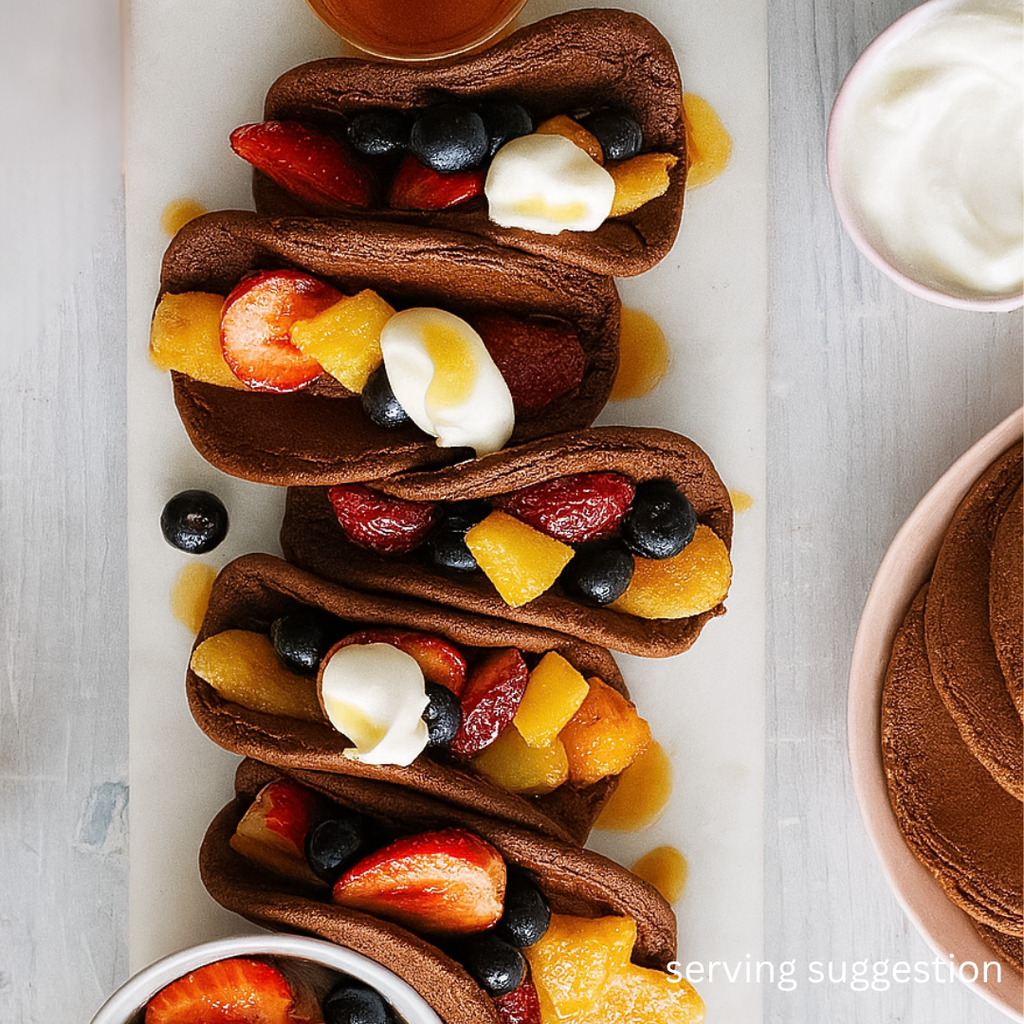 Chocolate protein SwoleCakes pancakes dessert with fruit on a white plate, surrounded by additional dessert items.