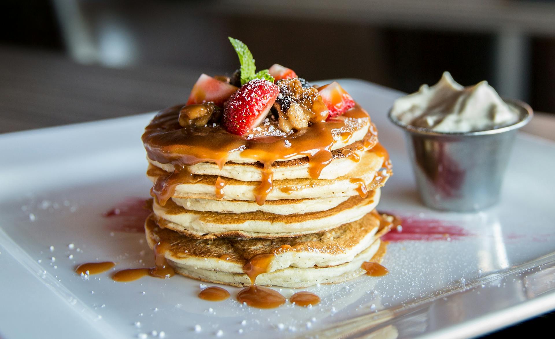 Stack of delicious protein pancakes with syrup, fruit, and whipped cream on a plate by SwoleCakes New Zealand & Australia. Buy Proetien Panckaes Online and Get Delivered to New Zealand and Australia.